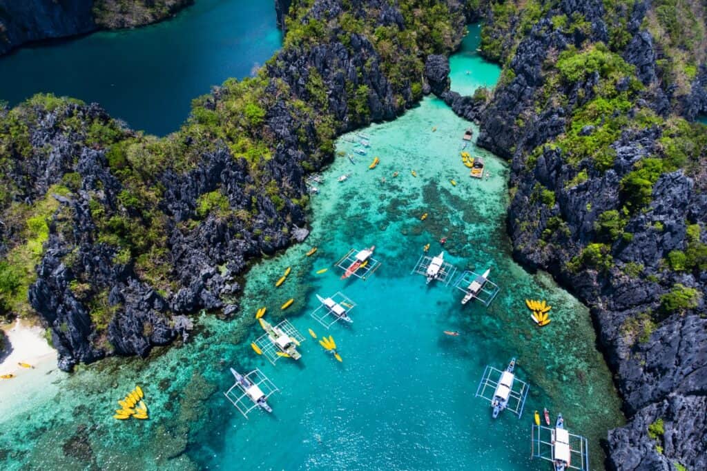 Big limestone formations surrounded with blue waters and docked small boats and kayak boats.