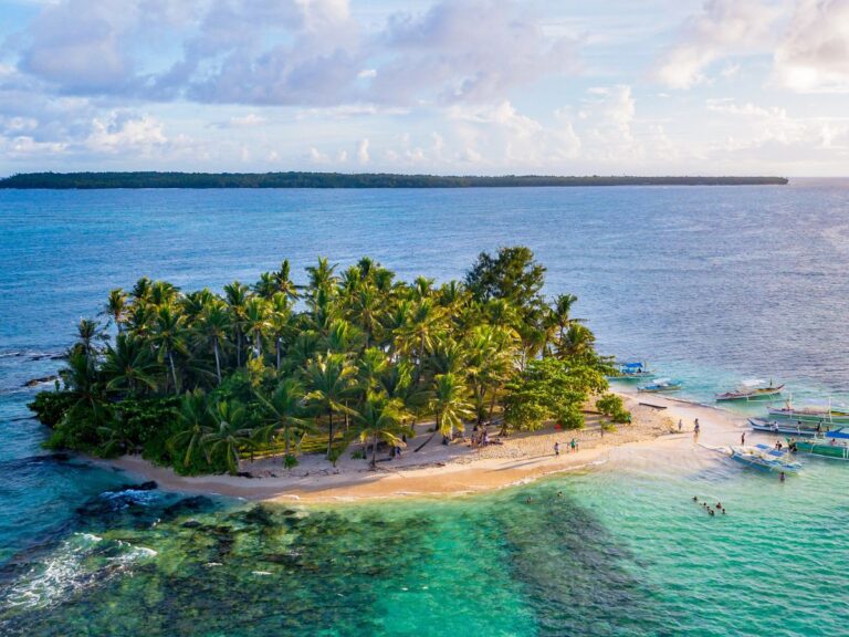 A small tropical island surrounded by clear blue water and palm trees, one of the stunning Hidden Islands of the Philippines.