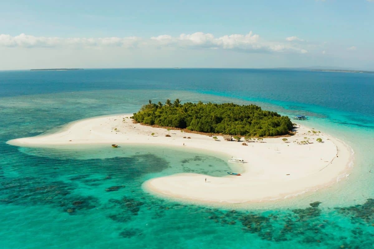 An aerial view of Balabac shows a pristine white-sand island surrounded by vibrant turquoise waters and coral reefs—one of the last untouched paradises in the Philippines. How to explore the Philippine islands