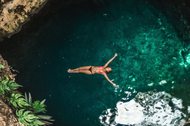 Woman in a red bikini floats serenely in the deep blue waters of Tayangban Cave Pool, representing the tranquil charm of the 7 Mystical Caves.
