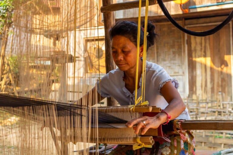 A woman is weaving on a loom in a village.