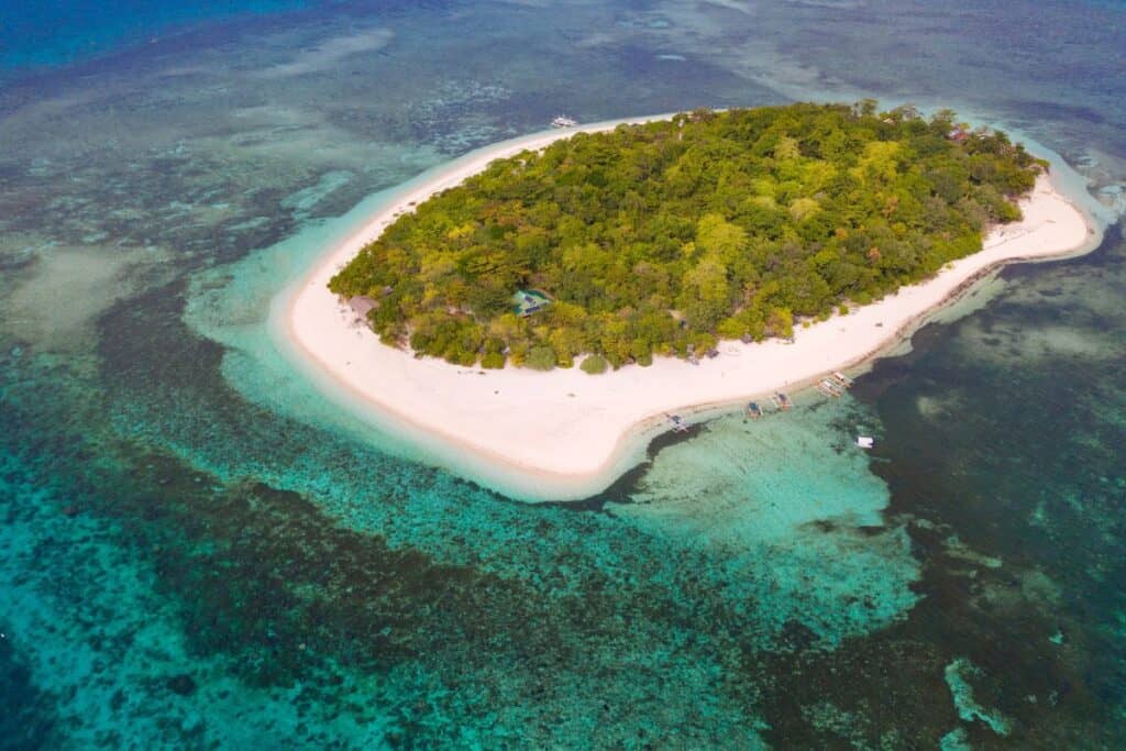 Secluded Philippine beach with white sand and clear turquoise waters, surrounded by lush tropical greenery.