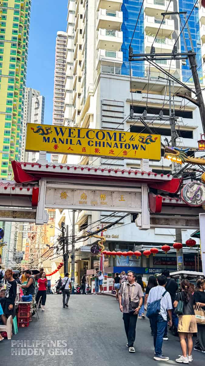 The "Welcome to Manila Chinatown" arch with tall buildings in the background.