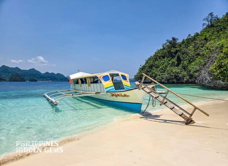 Cebu to Dinagat Island featured image of a boat on a white sand beach with clear skies and waters.