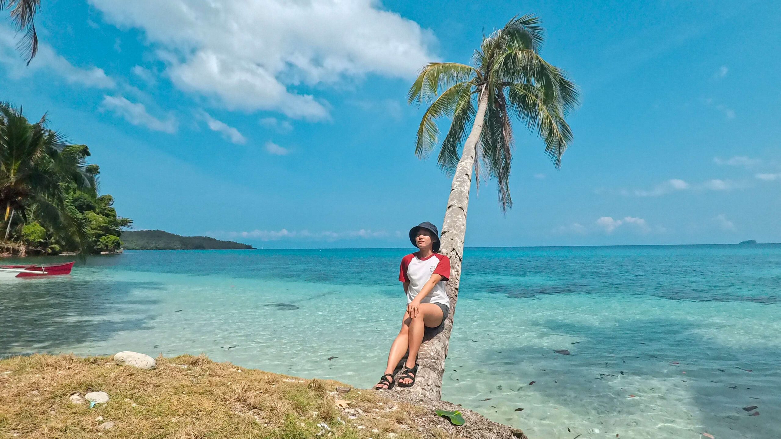 Kristine is sitting on a coconut with the view of the sea and Cabacongan Cove in Dinagat Island.