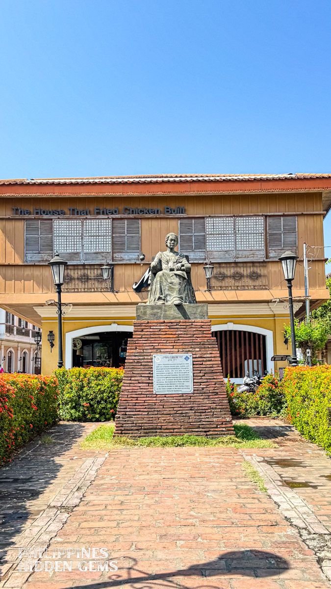 A statue of a woman in front of a restaurant with old Filipino house style architecture.