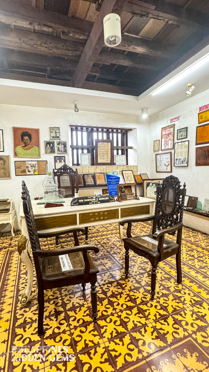 An old office with table, chairs, and framed photos and newspaper clippings.