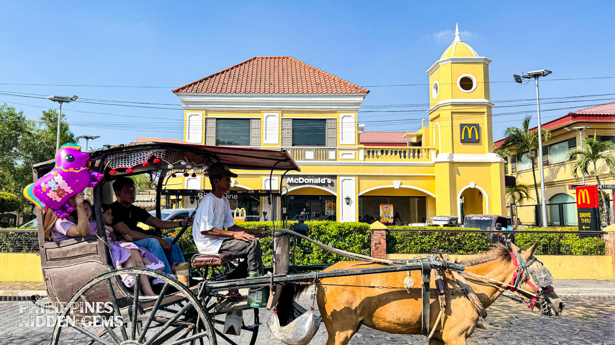 Four people riding a traditional Filipino horse-drawn carriage with a driver in the front controlling the horse.