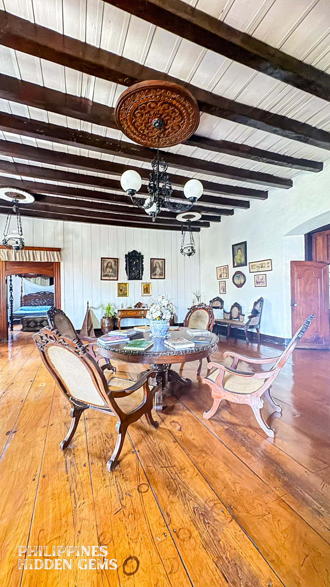 The living room of a Filipino Spanish-colonial home with circular table, chairs, and portraits on the wall.