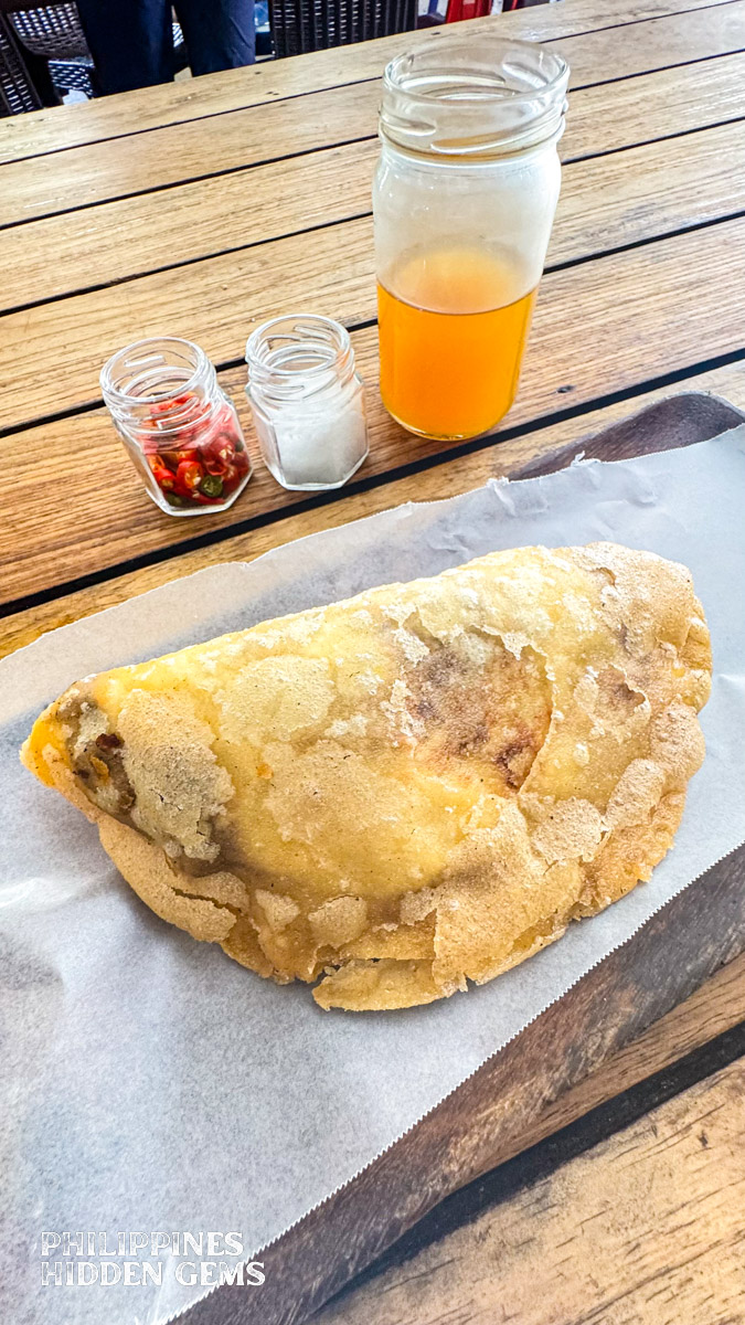 A wooden plate of Vigan Empanada, with condiments on the side.