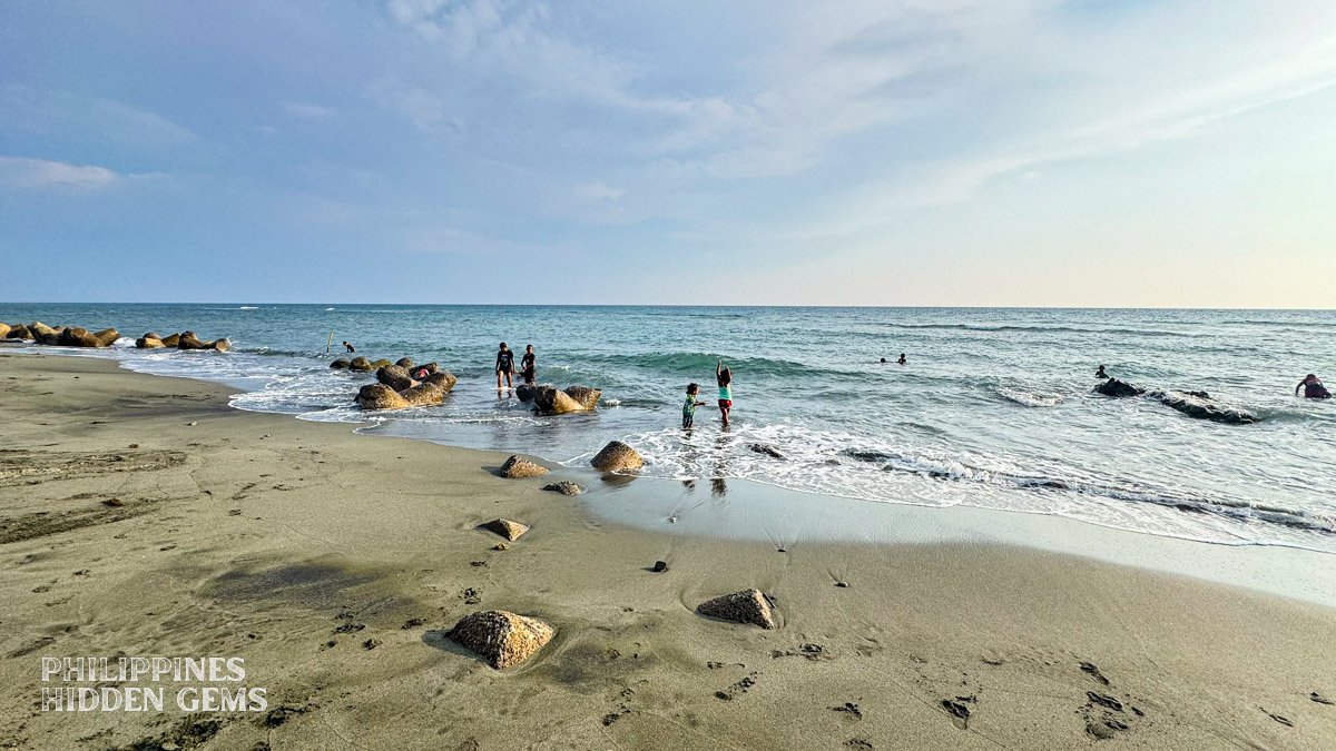 People playing and swimming at a dark-sand beach.