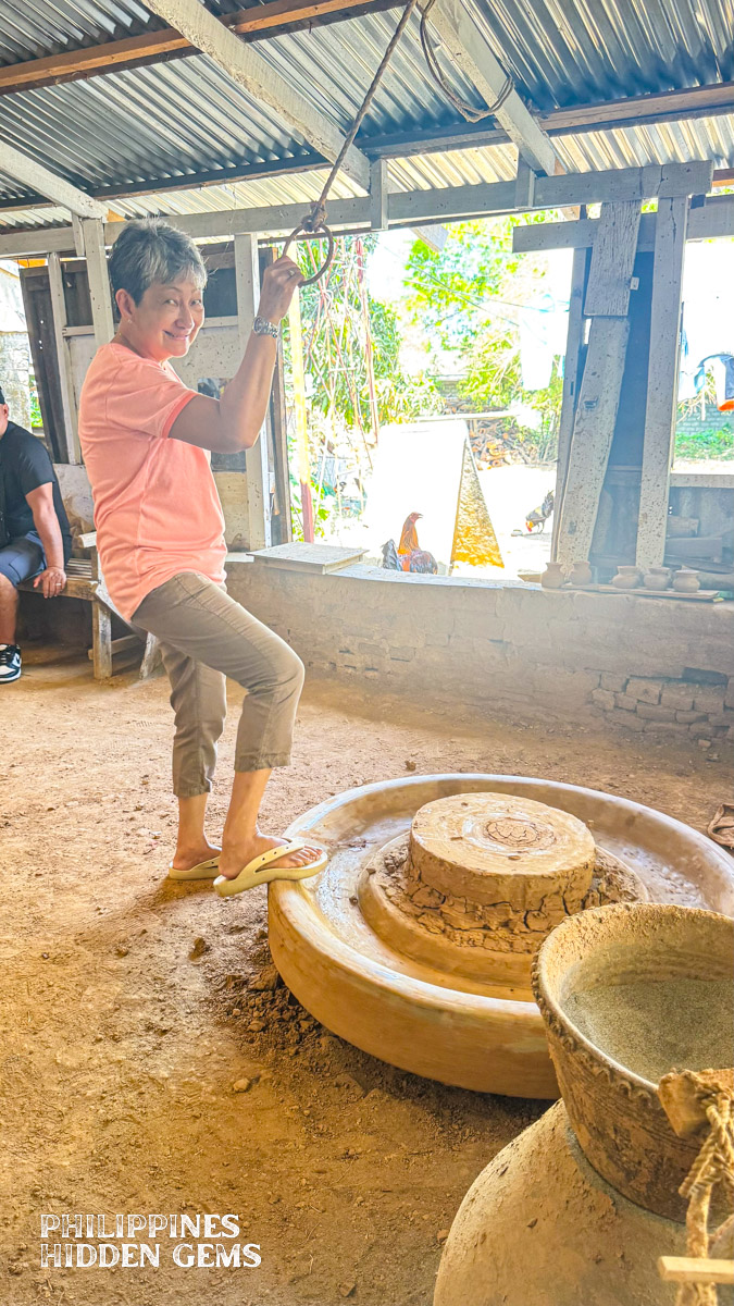A woman standing beside a traditional potter's wheel.