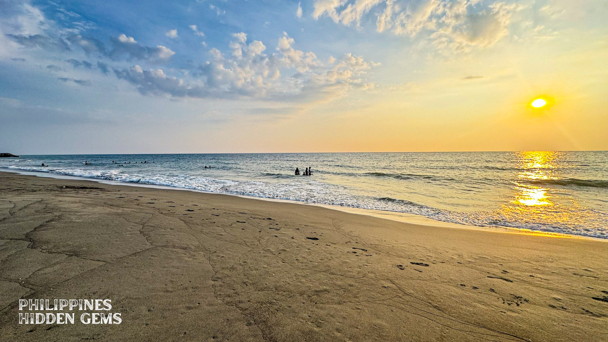 People swimming at a beach in Vigan at sunset.